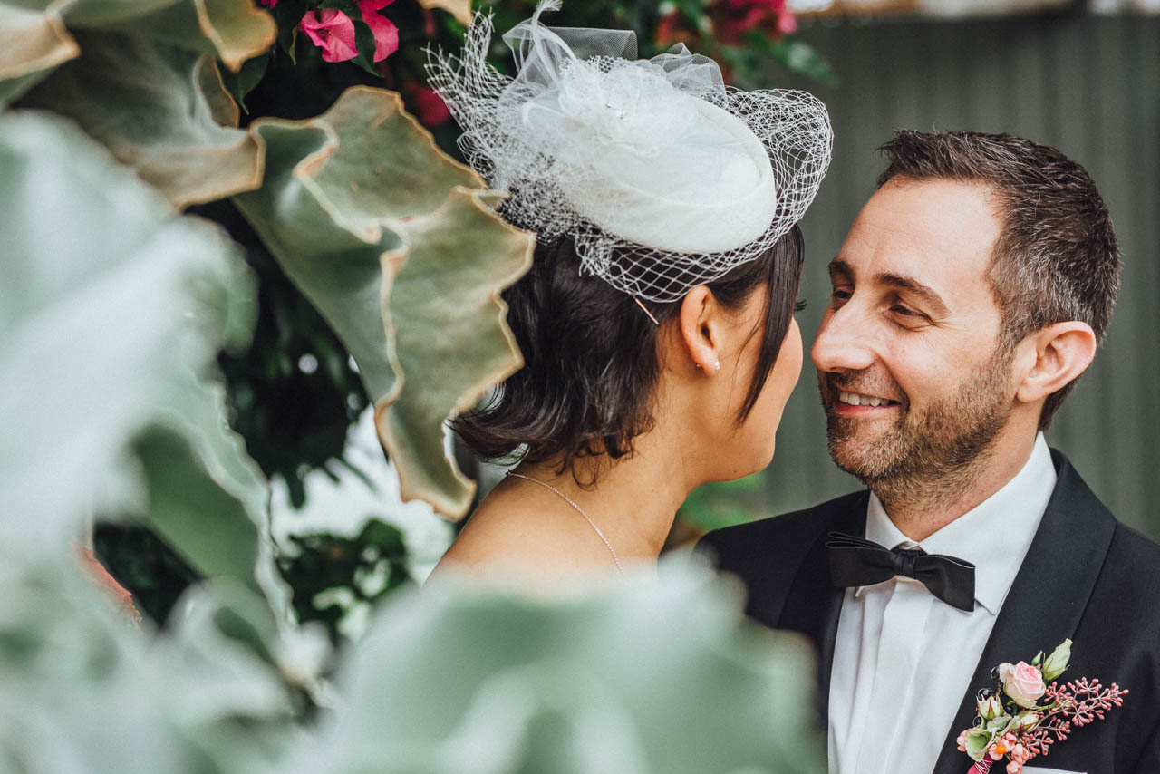 Braut mit Fascinator und Bräutigam im Smoking lachen sich an – Vintage Herbsthochzeit in München