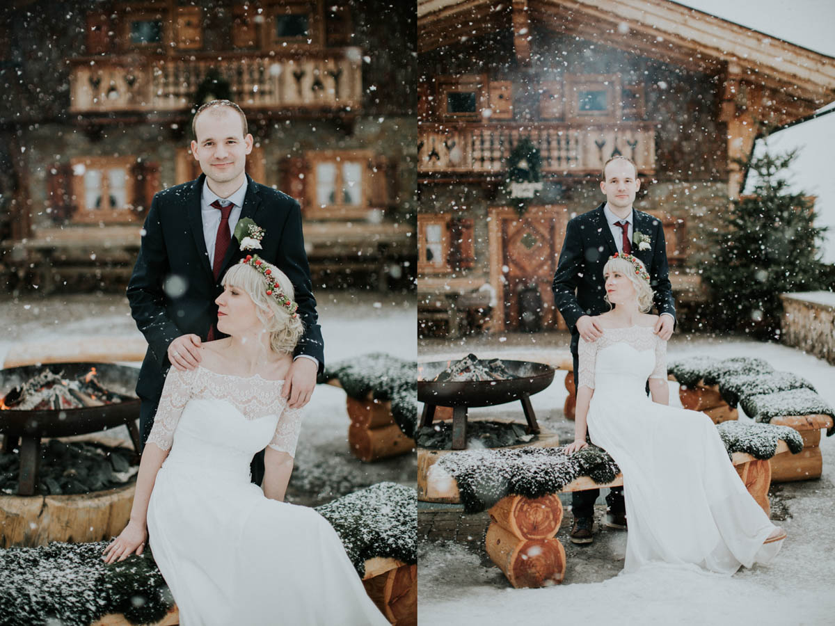 Bräutigam steht hinter Braut und die Schneeflocken rieseln auf sie herab