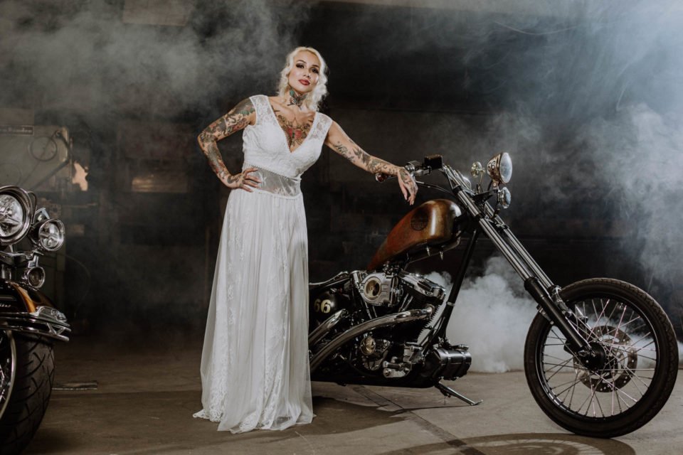 Motorrad Hochzeit - Rocker Braut im bauchfreien Brautkleid an Harley gelehnt