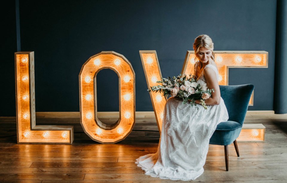 Braut sitzt vor leuchtenden LOVE Großbuchstaben aus Holz