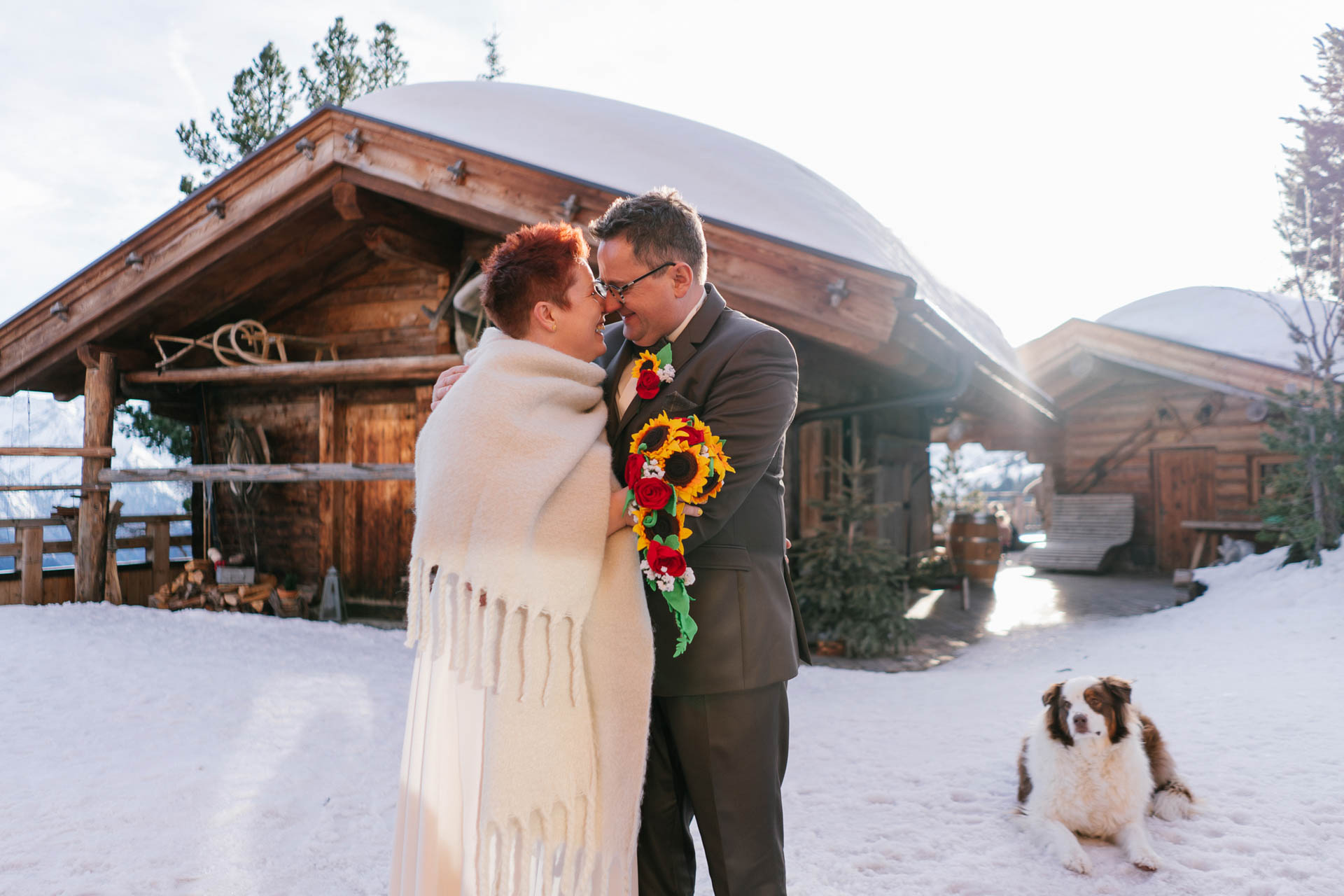  Brautpaar glücklich im Schnee neben Hund vor Schneekarthütte