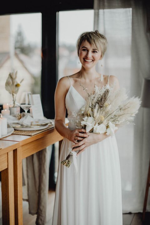 Glücklich strahlende Kurzhaar-Braut mit Trockenblumen