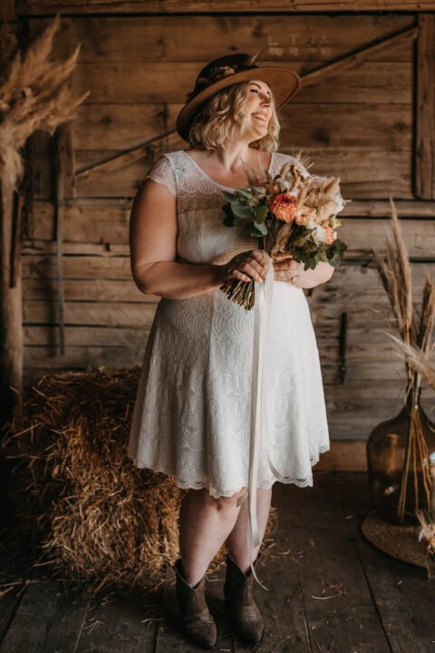 Lachende Braut im kurzen Plus Size Brautkleid mit Brautstrauß