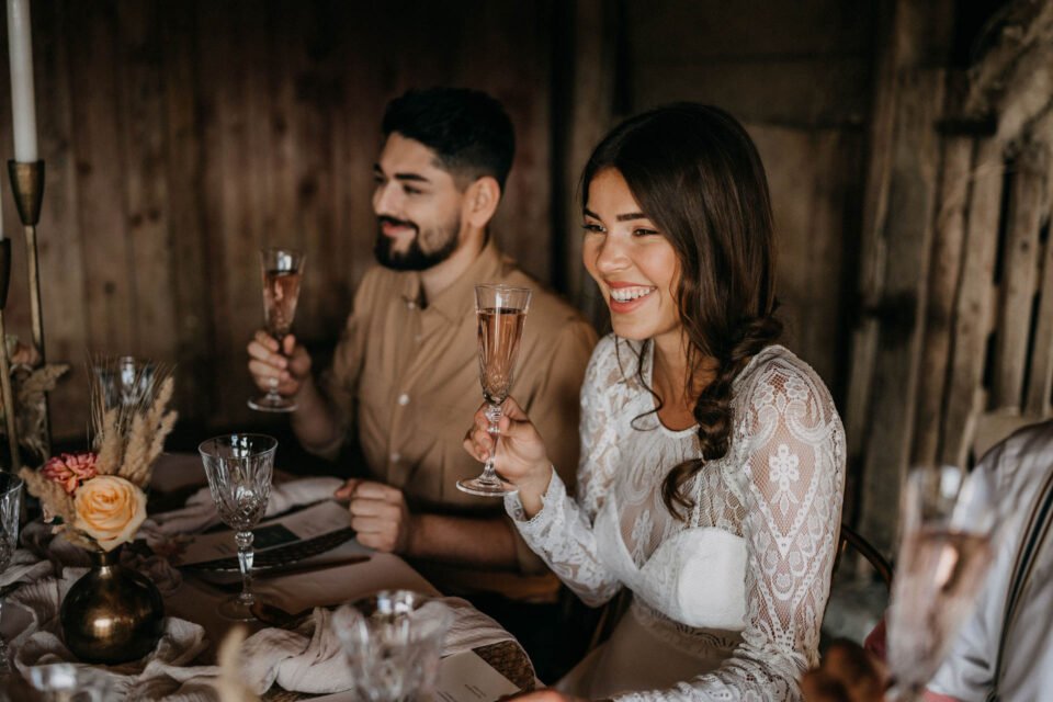 Braut und Bräutigam glücklich mit Sektglas in der Hand am Tisch