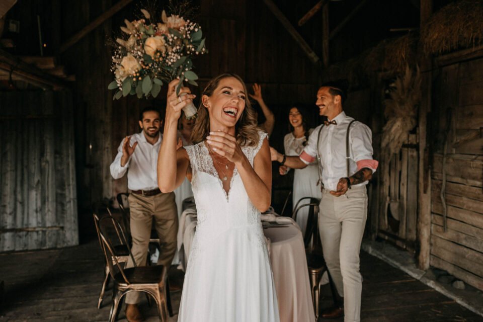lachende Braut schmeißt Brautstrauß in der Scheune