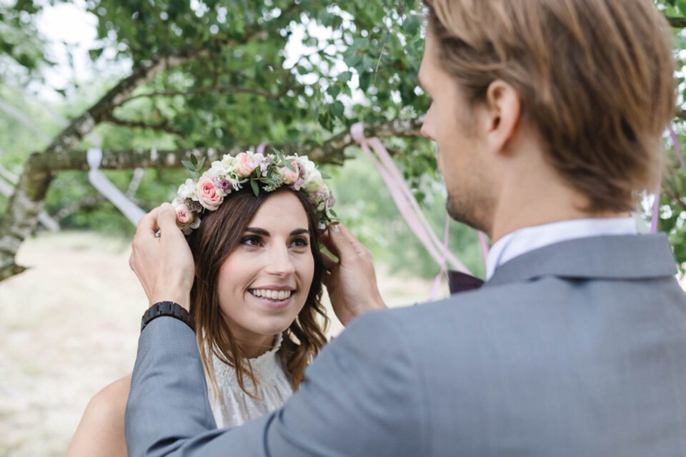 Bräutigam setzt strahlender Braut Blumenkranz in die Haare