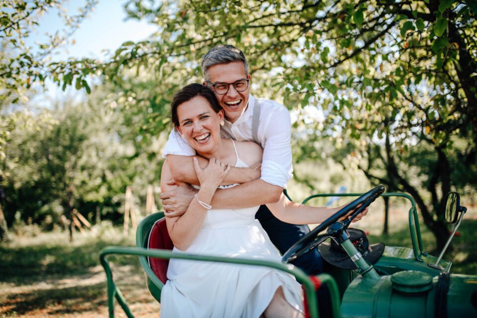 lachendes Brautpaar auf Traktor bei Gartenhochzeit