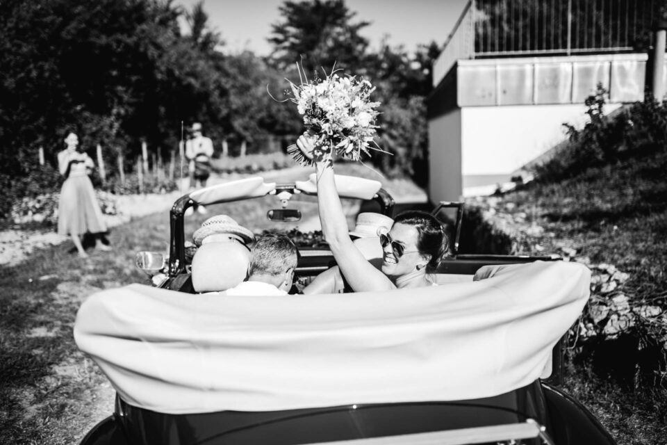 Brautpaar lässt sich im Cabrio nach Gartenhochzeit zur Hochzeitslocation fahren