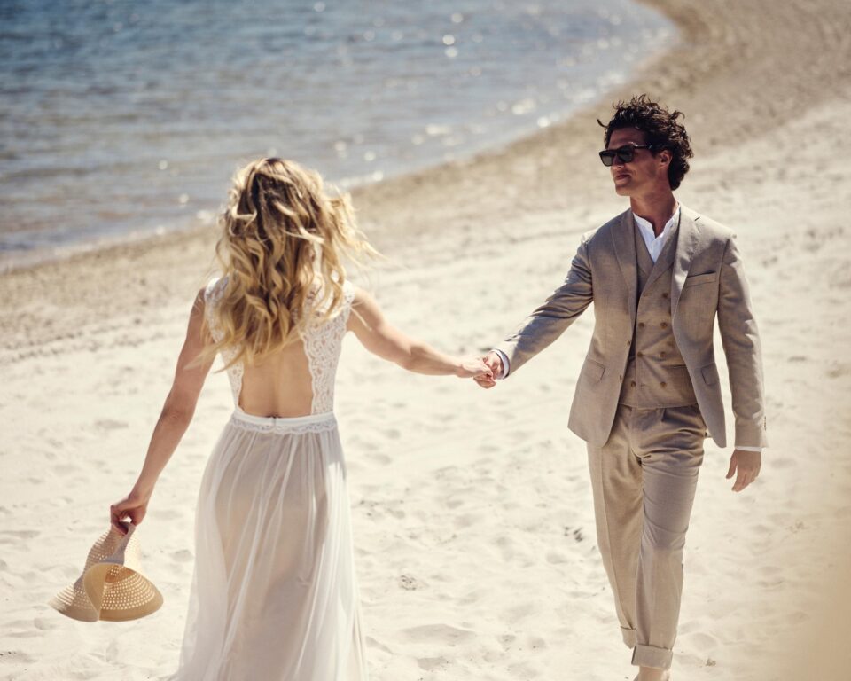 Boho Brautkleid rückenfrei am Strand, Braut und Bräutigam Hand in Hand