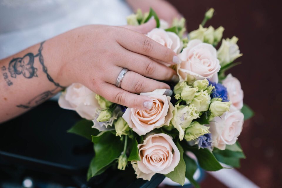 Detailaufnahme von Brautstrauß mit Rosen und tätowierter Braut mit Ehering 