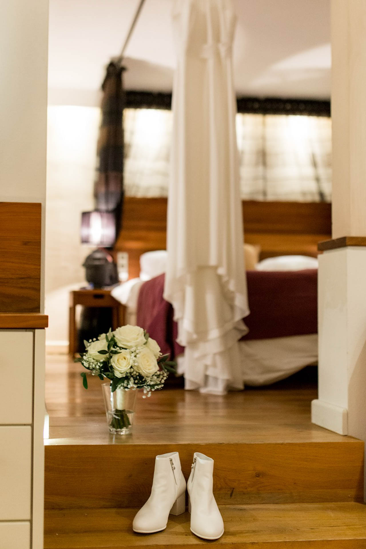 Schlichtes Brautkleid KUESSdieFINJA hängt im Hotelzimmer, davor weiße Stiefeletten und der Brautstrauß