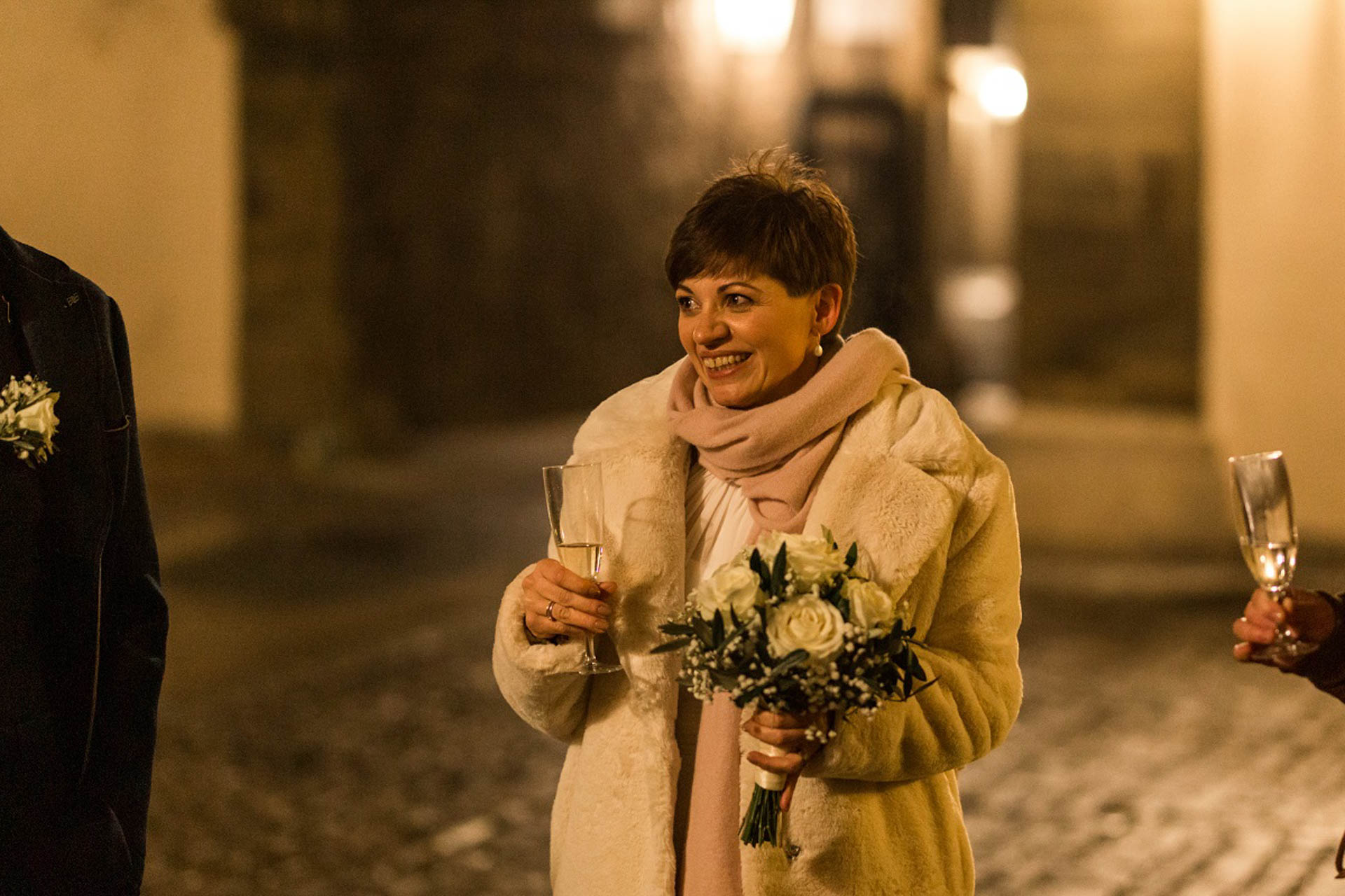 Braut im Teddymantel mit Sektglas nach der Candle-Light-Hochzeit im Freien