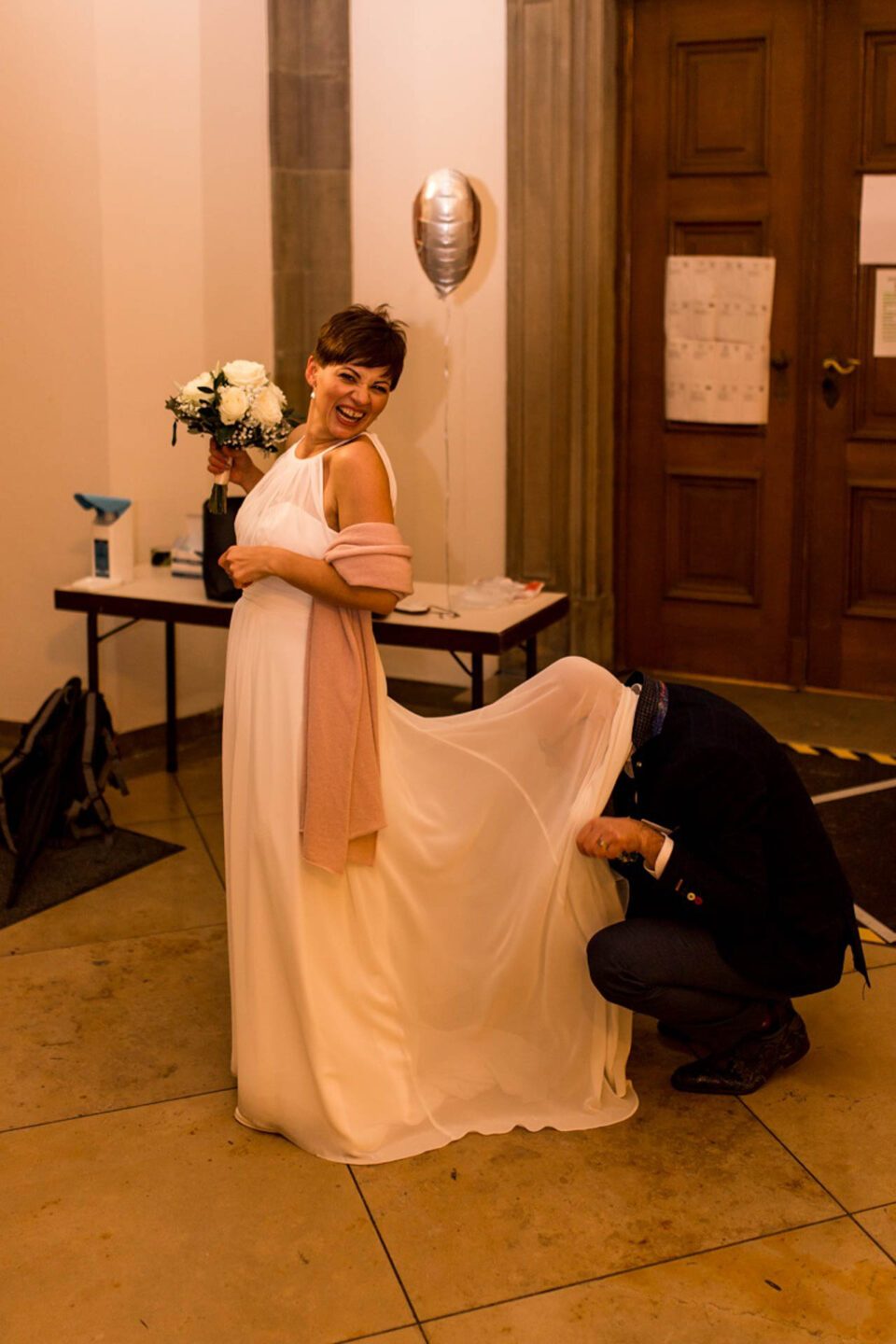 Bräutigam "versteckt" sich unter der Schleppe des Brautkleides in der Kirche, Braut lacht herzhaft