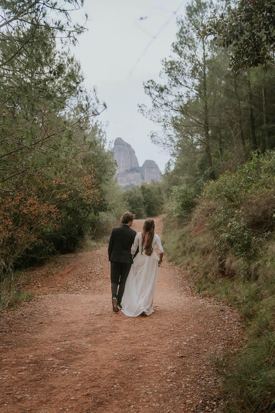 Brautpaar in Spanien von hinten fotografiert in Montsserrat zwischen Bäumen