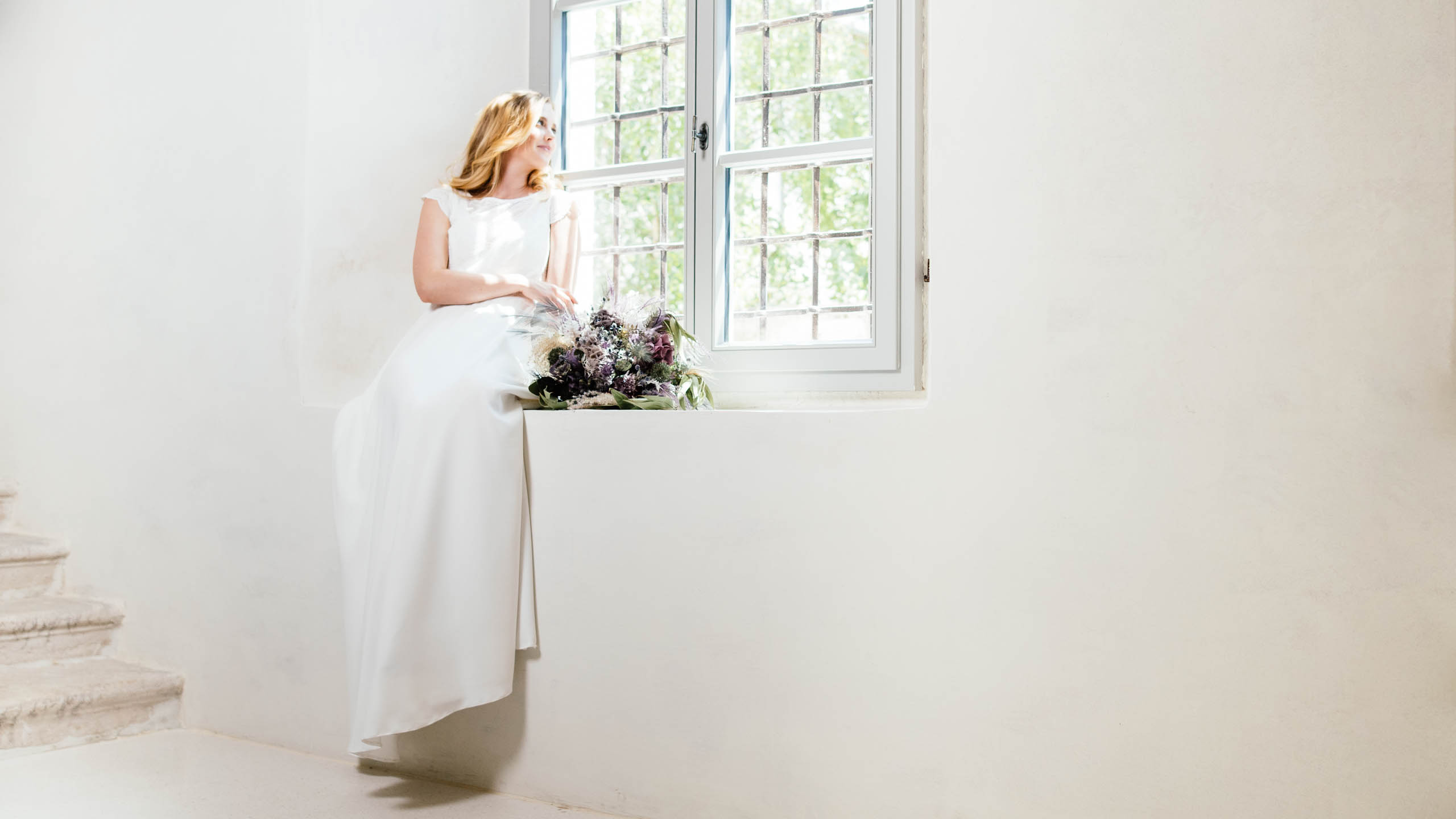 Braut im Hochzeitskleid schaut aus dem Fenster