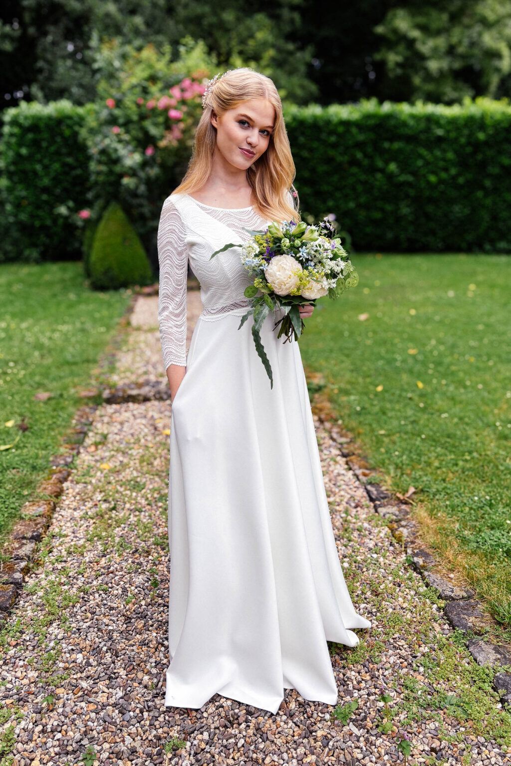 Braut mit Strauß im Kleid mit 3/4-Ärmeln aus Spitze im Garten